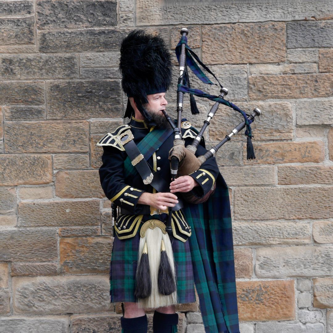 Scottish man wearing traditional tartan playing bagpipe outdoors